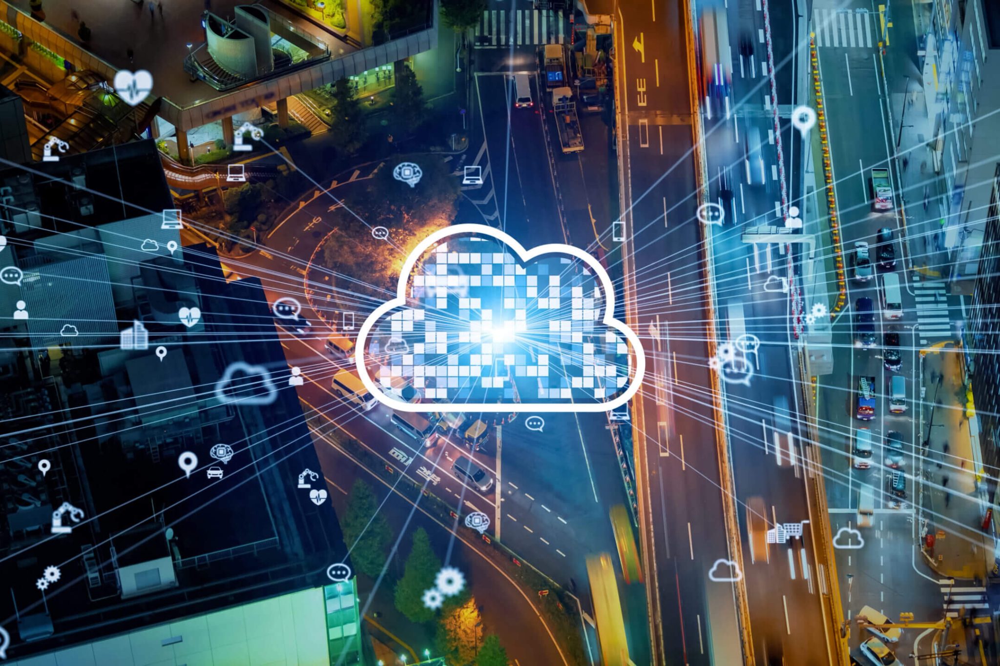 An illustration of a white and blue digital cloud in the sky overlooks a photo of a downtown city street with tall buildings at night. The interior of the cloud is made of a grid of small squares. The cloud has a burst of thin white lines shooting out from it, leading to various icons like a laptop and smart phone suggestive of our software integration platform.